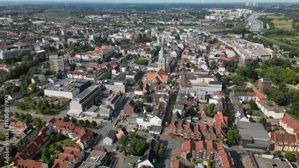 Obraz premium Aerial view of a European city with red-roofed buildings, a historic church, residential areas, and green surroundings. Ideal for urban, editorial, or architectural use.