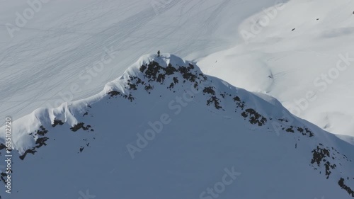 Aerial shot of skier standing on large snow-capped peak in Alaska about to drop in