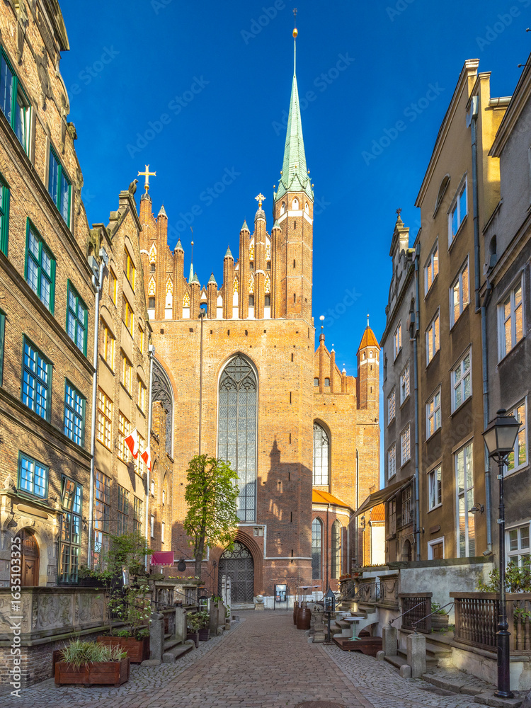 Fototapeta premium Gdansk, a city on the Baltic coast of northern Poland, Europe. Majestic cathedral towering over a charming cobblestone street, its spire reaching into the clear blue sky in an old European city.