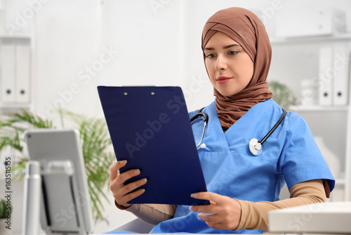 Female Muslim doctor with clipboard in clinic