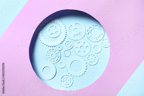 Figures of gears on blue background visible through cut lilac paper