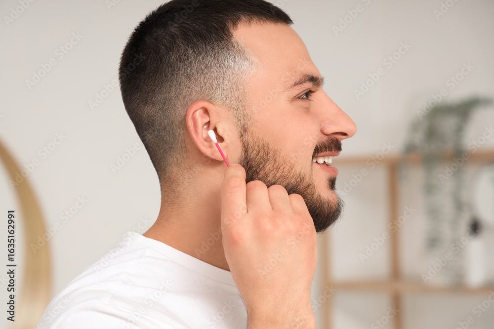 Fototapeta premium Young man cleaning ears with cotton bud in bathroom