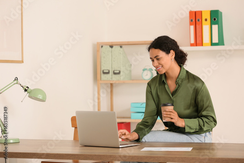 Beautiful young African-American businesswoman working with modern laptop and...