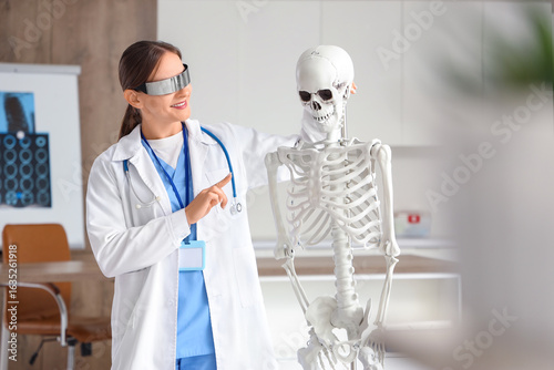 Female doctor in goggles examining human skeleton model at hospital