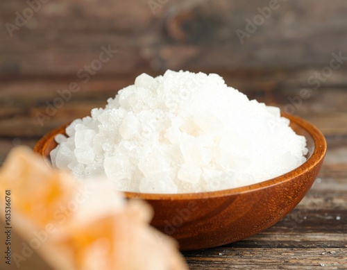 a pile of sugar in a bowl, with sugar grains scattered on the table.