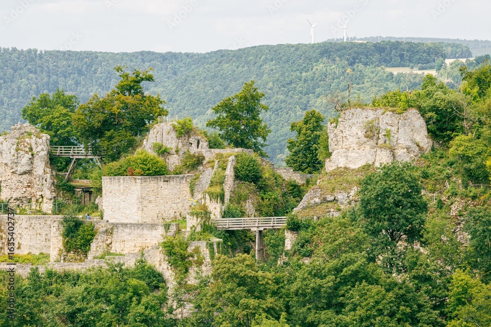 Fototapeta premium Ruins of a medieval castle surrounded by lush greenery in a hilly landscape