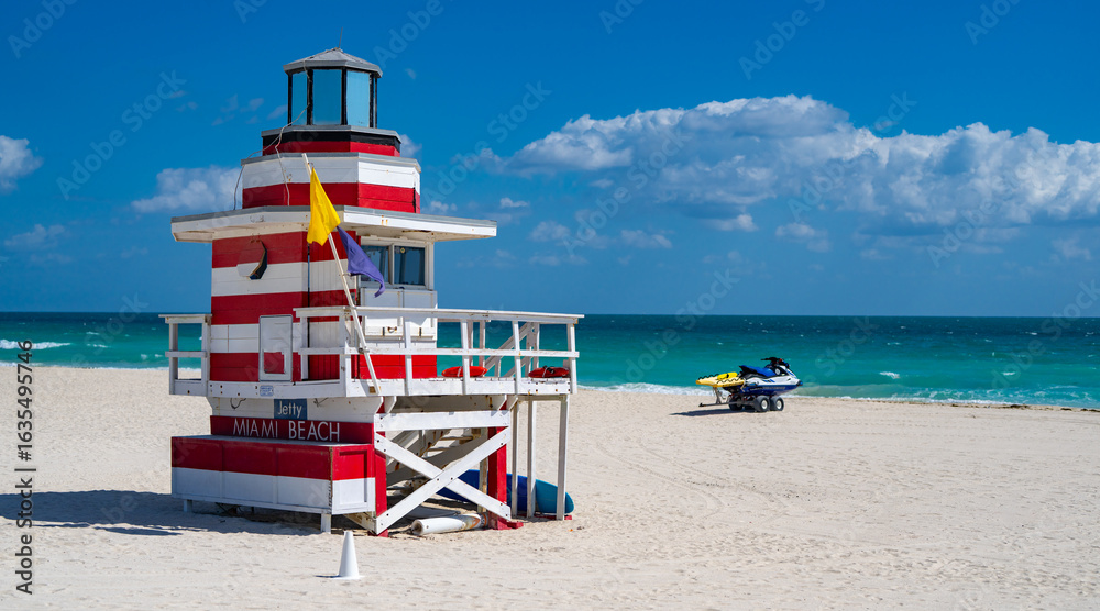 Fototapeta premium Miami Beach lifeguard at the summer beach. South Miami Beach with lifeguard. Sky above lifeguard tower in Miami. Iconic lifeguard tower on sand in Miami. A symbol of Miamis coast.