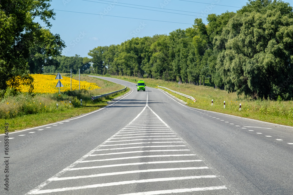 Fototapeta premium Rural road with green van near sunflower field