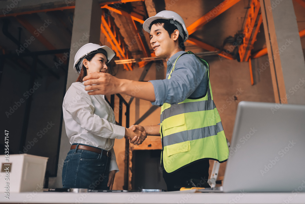 Fototapeta premium Construction manager and engineer dressed in orange work vests and hard helmets explore construction documentation on the building site near the steel frames