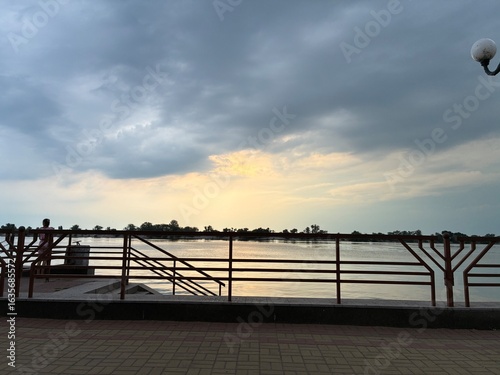Peaceful photo of a river promenade with railings and dramatic sunset sky, taken in Ukraine