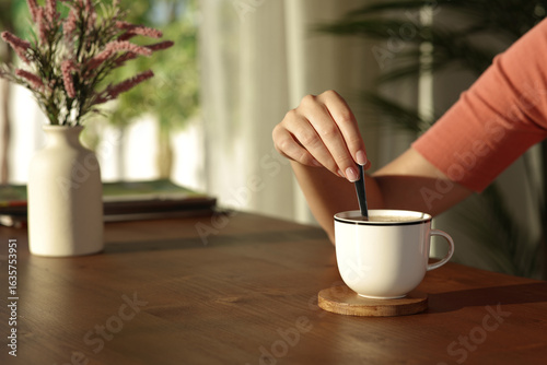 Woman hand at sunset at home stirring coffee