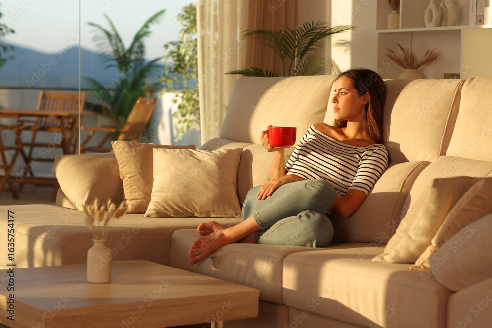 Obraz premium Woman relaxing drinking coffee from red cup at home at sunset
