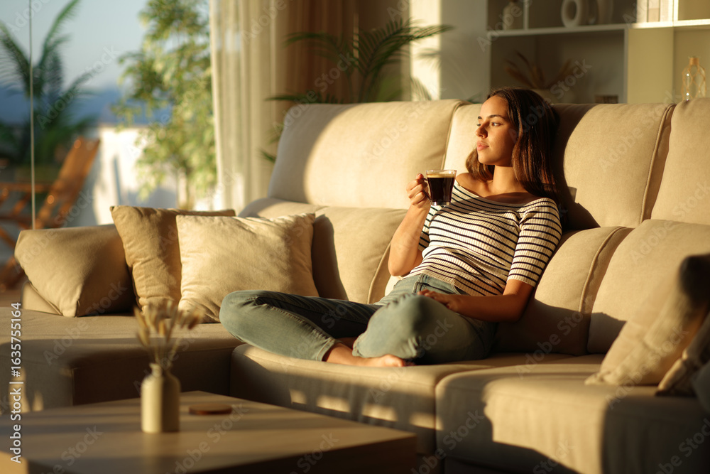 Obraz premium Woman drinking coffee at sunset relaxing on a couch at home