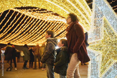 Photos Mother with two sons admiring Christmas lights at festive outdoor market