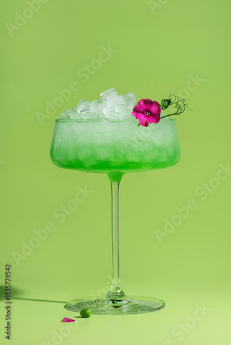 Stylish green gradient cocktail in a tall glass with crushed ice decorated with pink phlox flower and pea microgreens garnish. Green background. Food styling of drinks. Bar and mixology concept