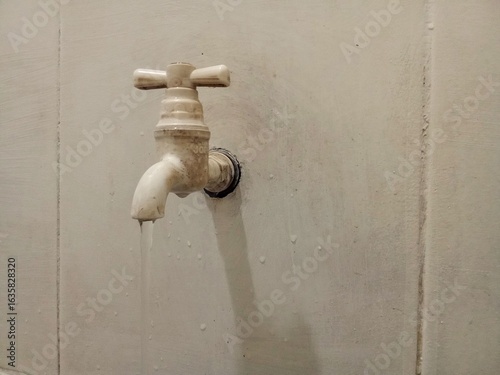 A detailed view of an old water faucet slightly open, letting a small stream drip