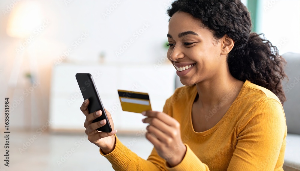 Fototapeta premium Smiling young African American woman sitting comfortably on floor at home, using smartphone and holding credit card. Relaxed mood, secure mobile banking, modern e-commerce lifestyle