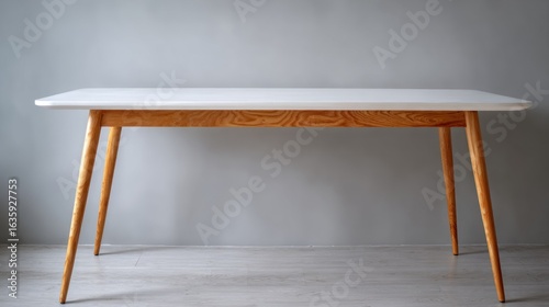 Minimalist white table with wood legs against a gray wall, bright neutral lighting