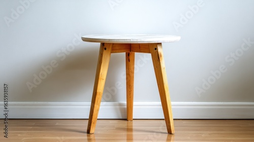 Small wooden stool with round top, against white wall and wood floor