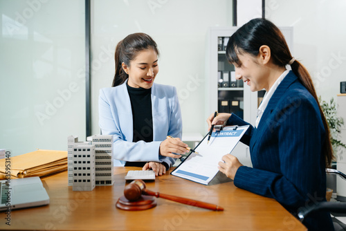 Two professional women reviewing a real estate contract with gavel, building model, and paperwork. Business law, legal advice