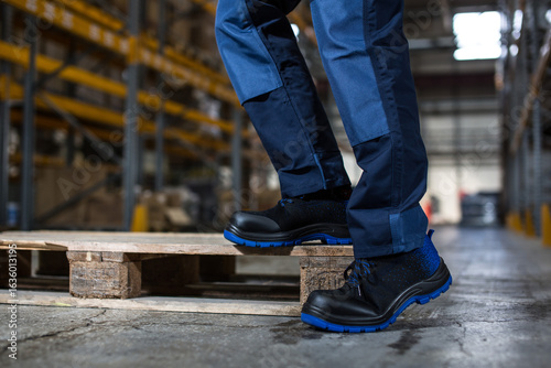 Foto Warehouse Worker in Safety Shoes Standing on Wooden Pallet
