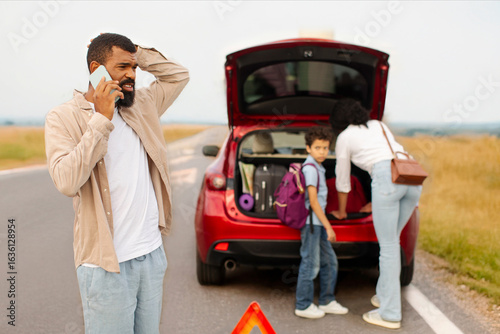 Fotografi Family near broken down car on their way to vacation, man calling on cellphone w