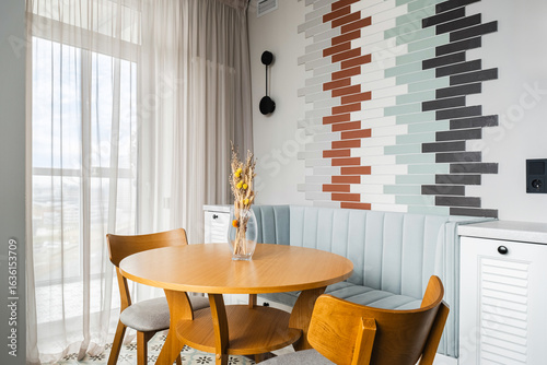 Modern dining area with a cozy round table and colorful accent wall in a well-lit interior space