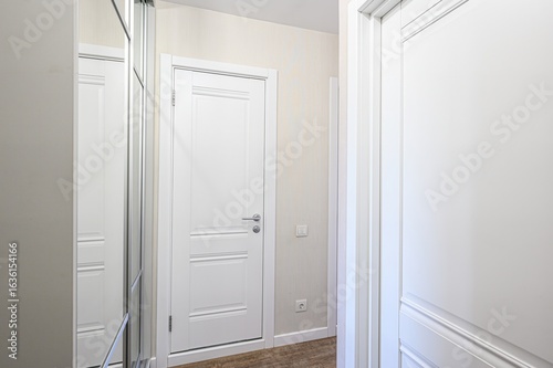 bright interior features two white doors and a mirrored closet. Walls are beige