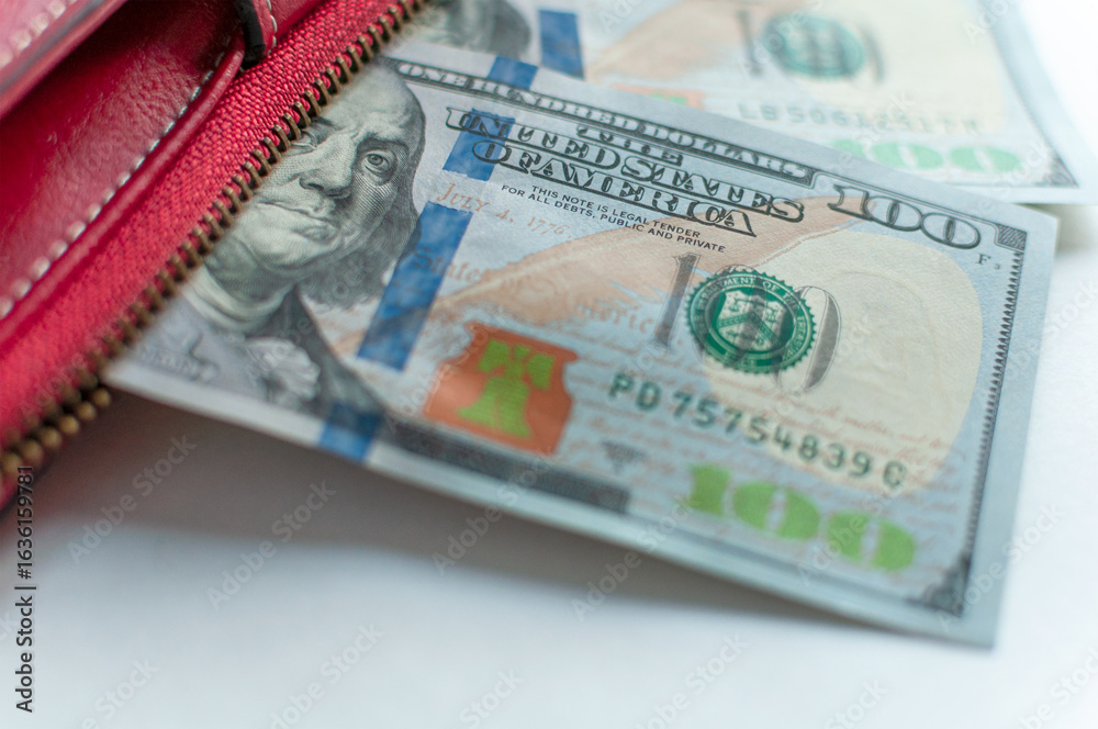Fototapeta premium The close-up image shows US$100 bills partially located in a red wallet. The details of the banknotes are visible, including the portrait of Benjamin Franklin.