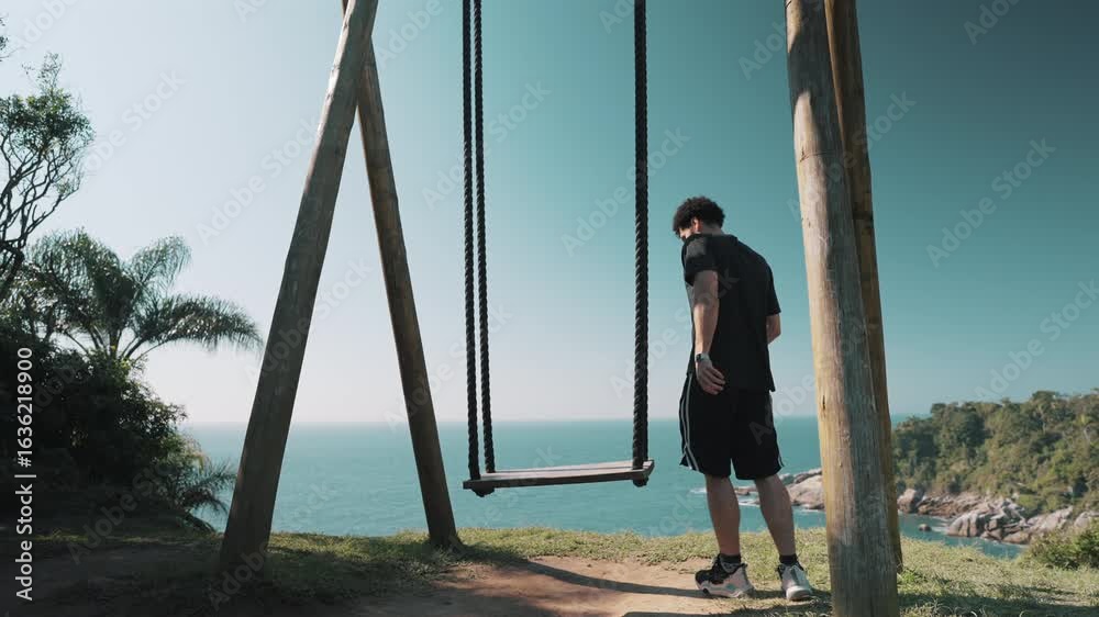 Man sits alone on wooden swing overlooking ocean, embracing solitude, mindfulness, and healing calm of nature Man sits alone on wooden swing overlooking ocean, embracing solitude, mindfulness, and healing calm of nature