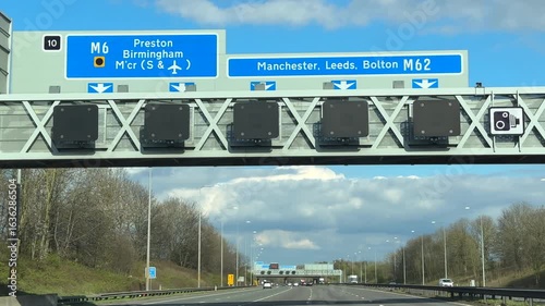 Driving motorway towards Manchester on M62, J10, junction 10, gantry information directional sign to M6, Manchester, Birmingham, Leeds, Bolton, Manchester airport, Preston, slow motion.