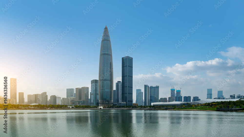 Naklejka premium Modern city skyline with tall skyscrapers and reflective lake under clear blue sky