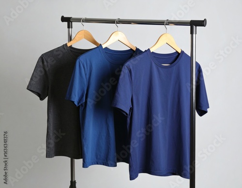 A collection of plain t-shirts in shades of blue and grey hanging on a clothing rack. A simple and stylish assortment of basic apparel for a minimalist wardrobe.