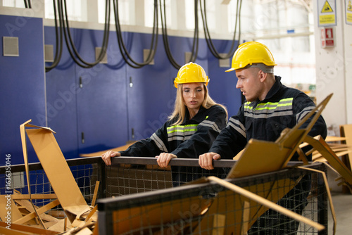Fotografie Male and female factory workers wearing safety gear checking cardboard waste in industrial bin
