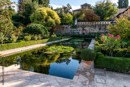 Alhambra complex in Granada town, Andalusia, Spain. Serene garden with a pond, lush greenery, and vibrant flowers.