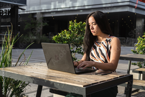 Young asian freelancer woman working on laptop outdoors in urban setting