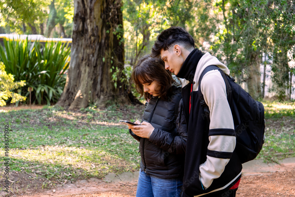Fototapeta premium Students using smartphone in park, exploring nature and technology