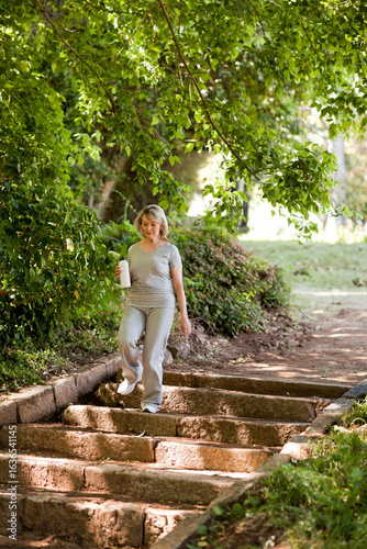 Fotografie Senior woman descending stone steps in park wearing gray athletic wear, holding