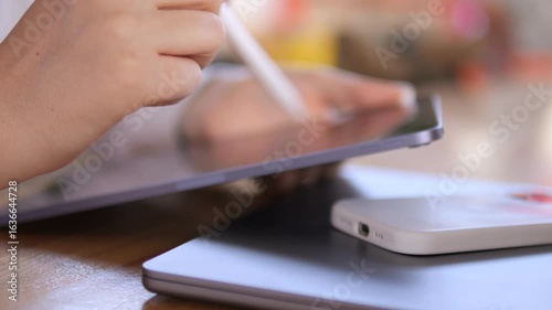 Person is writing on a tablet with a white pen. A cell phone is on the table next to the tablet
