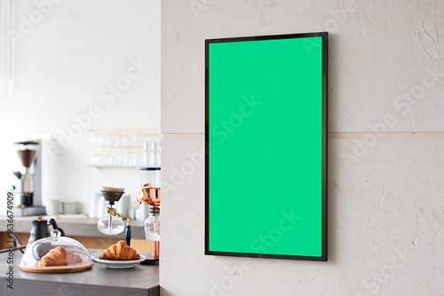 A blank vertical green screen frame mockup hanging on a wall in a modern cafe.
