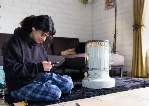 Tableau sur toile teenage girl sitting on the living room floor next to a kerosene stove heater