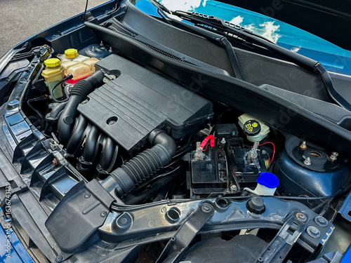 A closeup image of a car engine compartment highlights its essential components and wiring, showcasing the complexity of automotive engineering and related repairs and maintenance