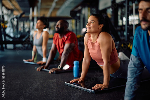 Happy athletic woman doing Sun Salutation exercise during group gym workout.