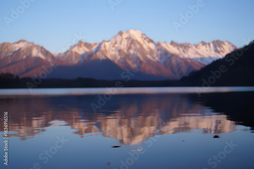A majestic snow-capped mountain range perfectly reflected in a tranquil lake at sunrise, creating a serene and beautiful landscape.