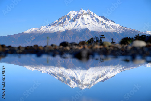 Majestic snow-capped mountain peak perfectly reflected in the tranquil, still water of a lake on a clear sunny day.