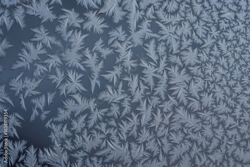 Intricate ice frost patterns forming on a cold glass window during winter. Abstract natural background of frozen water crystals.