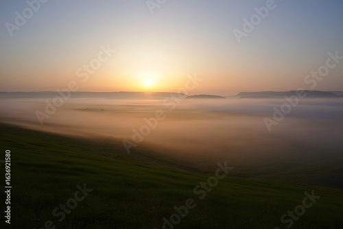 Golden sun rising above a thick blanket of morning mist covering a picturesque green landscape.