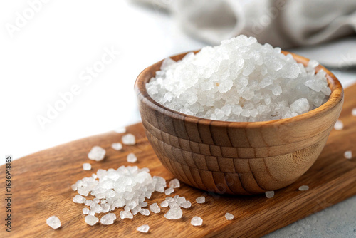 Coarse sea salt in a wooden bowl. Close-up of natural rock salt crystals on a wooden board, a key ingredient for cooking and seasoning.