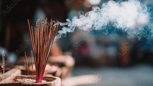 Burning incense sticks emit wispy smoke, creating a serene and spiritual atmosphere. The background is blurred, focusing attention on the fragrant smoke and the burning incense in a holder