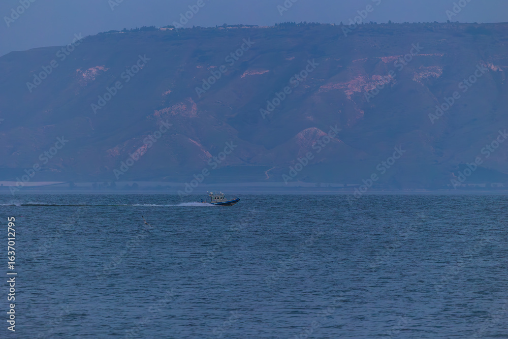 Obraz premium Evening twilight views of the Sea of Galilee in Israel with calm waters, distant mountains, boats, and serene blue tones creating a peaceful atmosphere